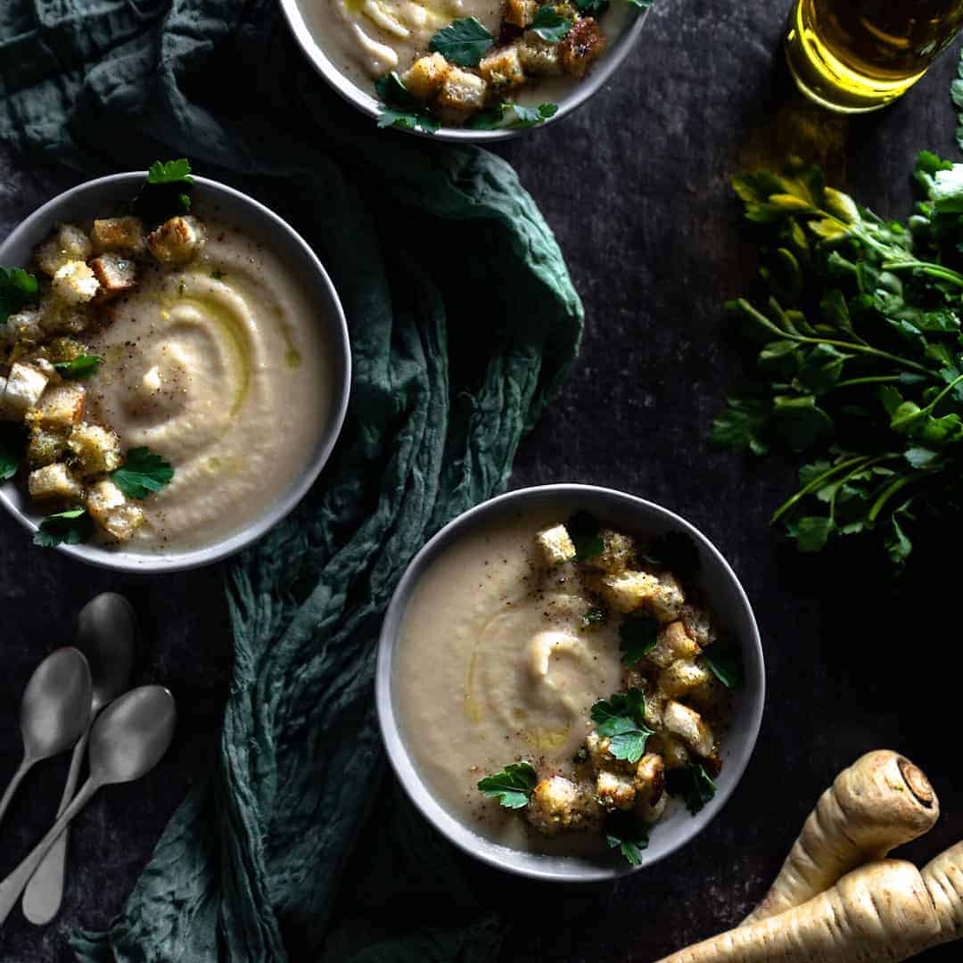 3 bowls of parsnip soup on a dark wood table