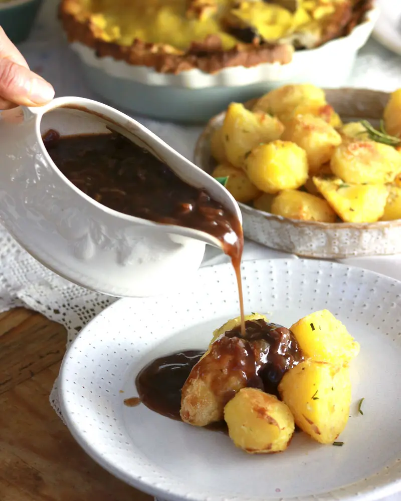 a gravy bowl filled with gravy being poured over potatoes