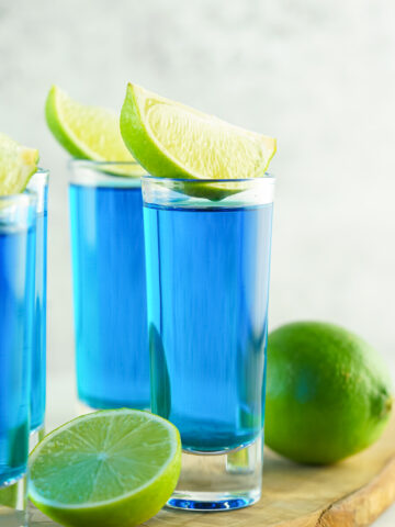 side view of blue kamikaze shot in a shot glass with wedge of lime