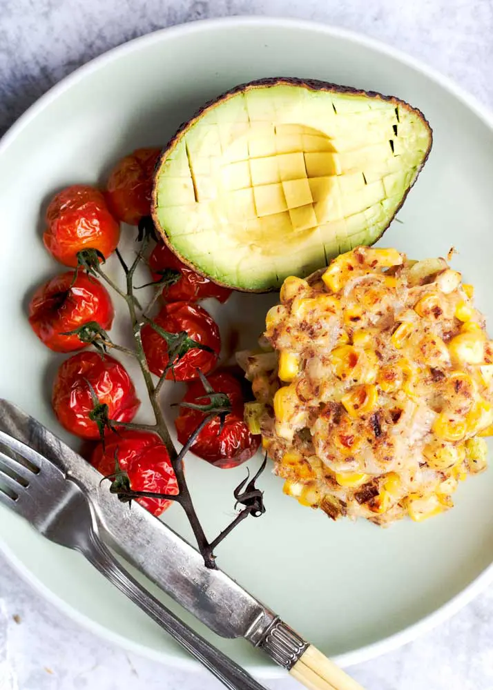 corn fritters on a white plate with roasted tomatoes and avocado