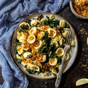 overhead view of a plate full of pasta with kale on a wood table