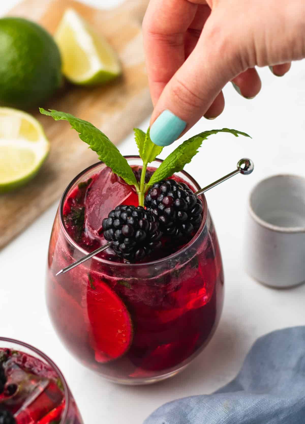 hand placing mint leave in a blackberry mojito