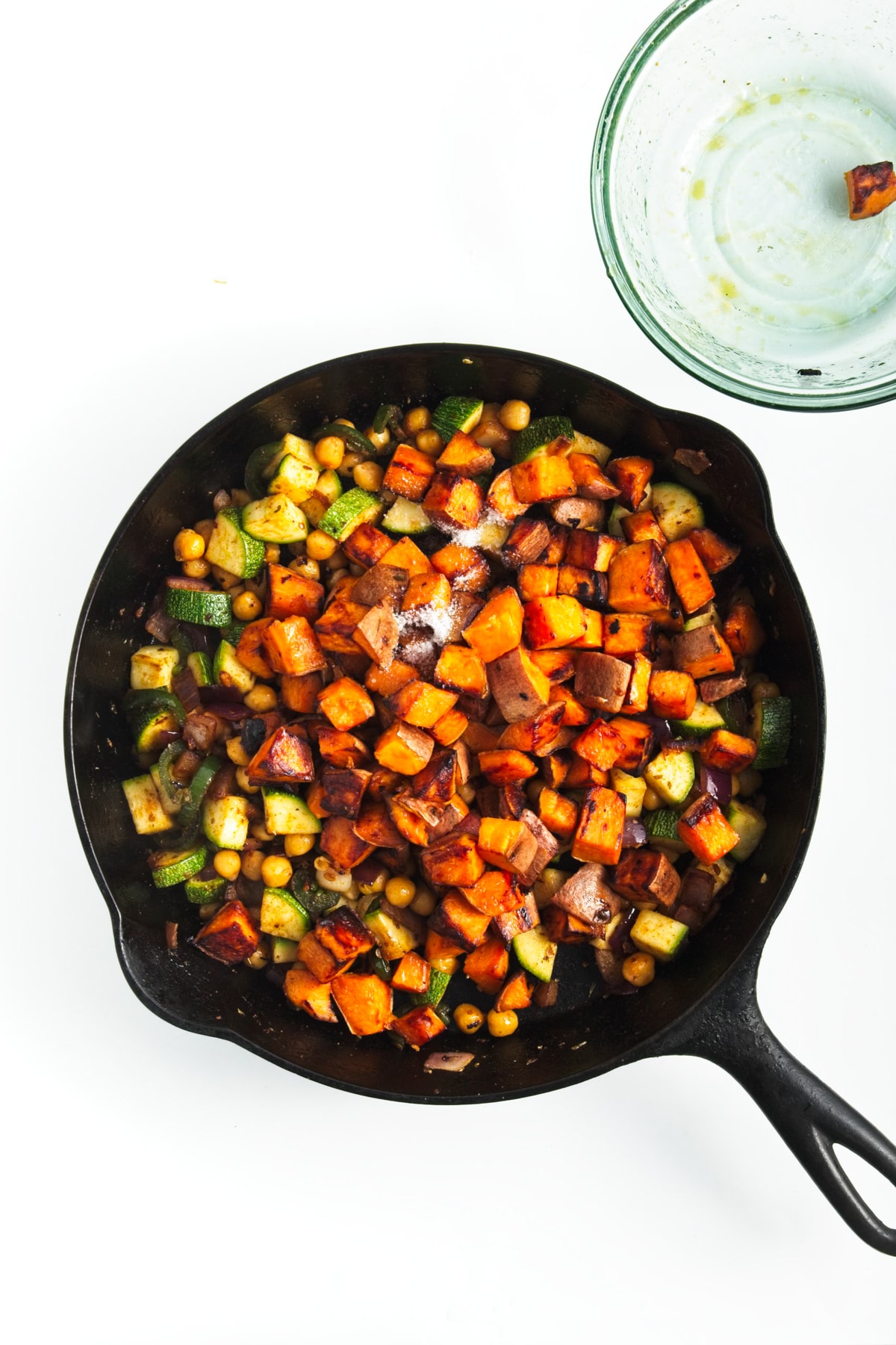 chopped sweet potatoes added to the veggies in a black skillet
