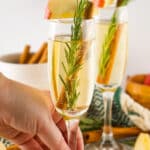 hand grabbing an apple cider mimosa off a white table