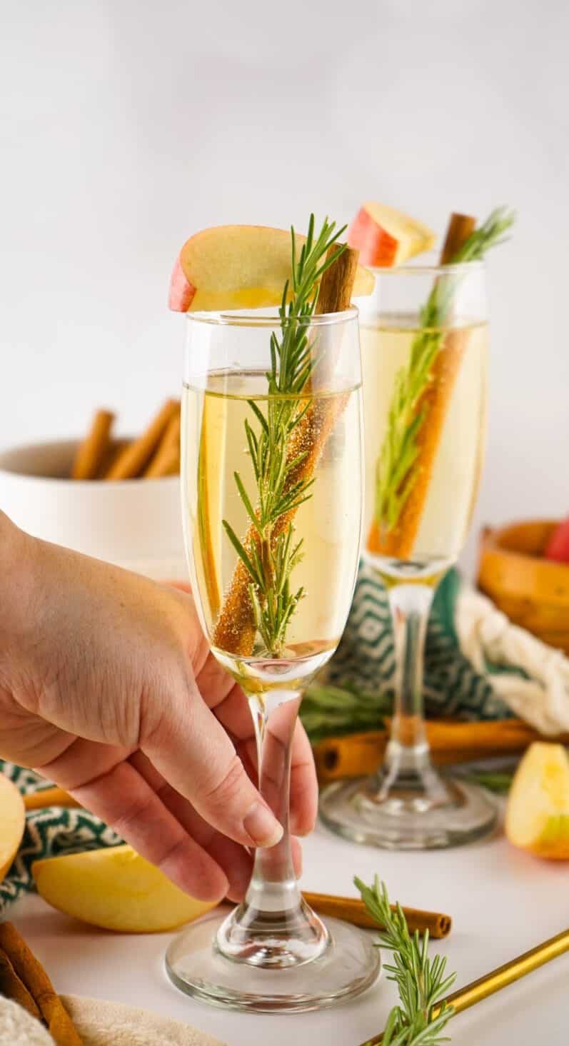 hand grabbing an apple cider mimosa off a white table