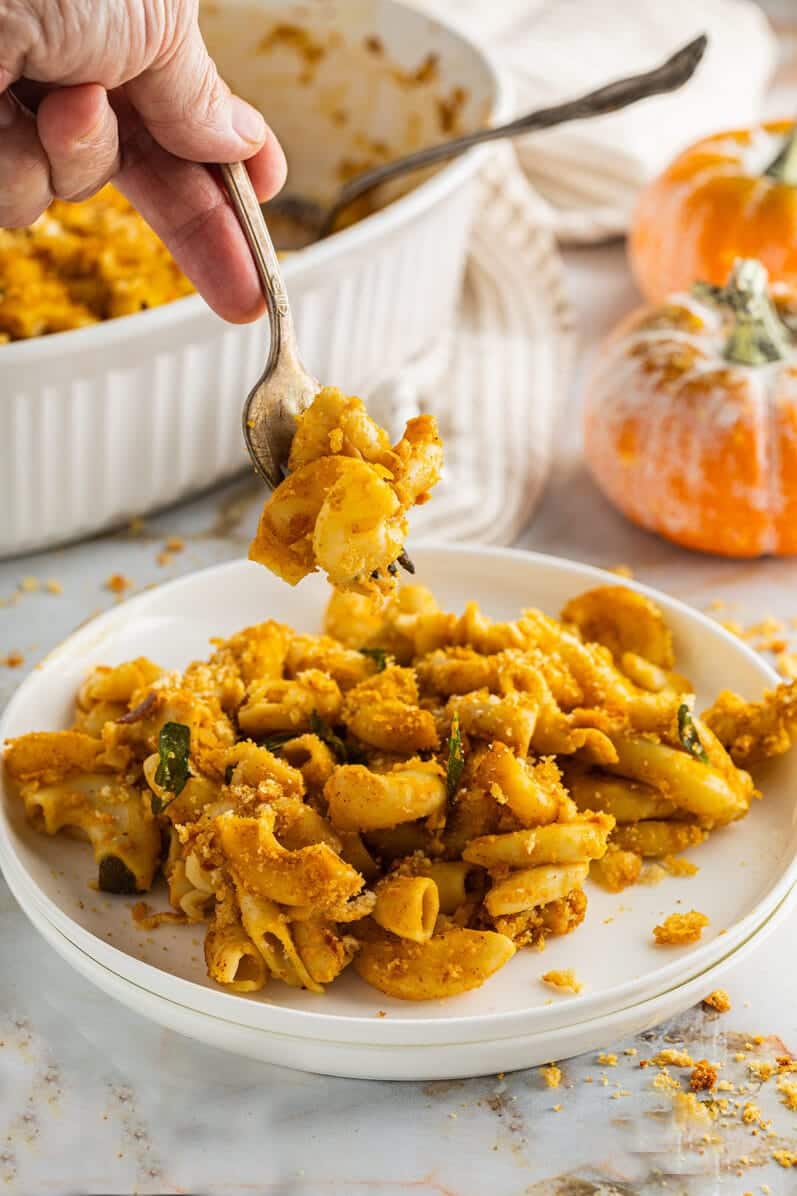 hand lifting a forkful of vegan pumpkin mac and cheese bake