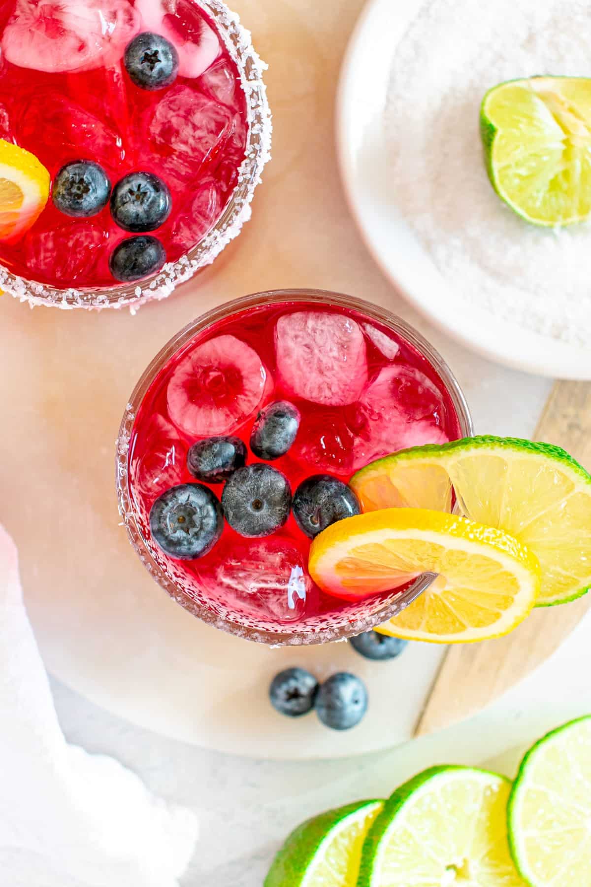 overhead view of 2 blueberry margaritas garnished with citrus and berries