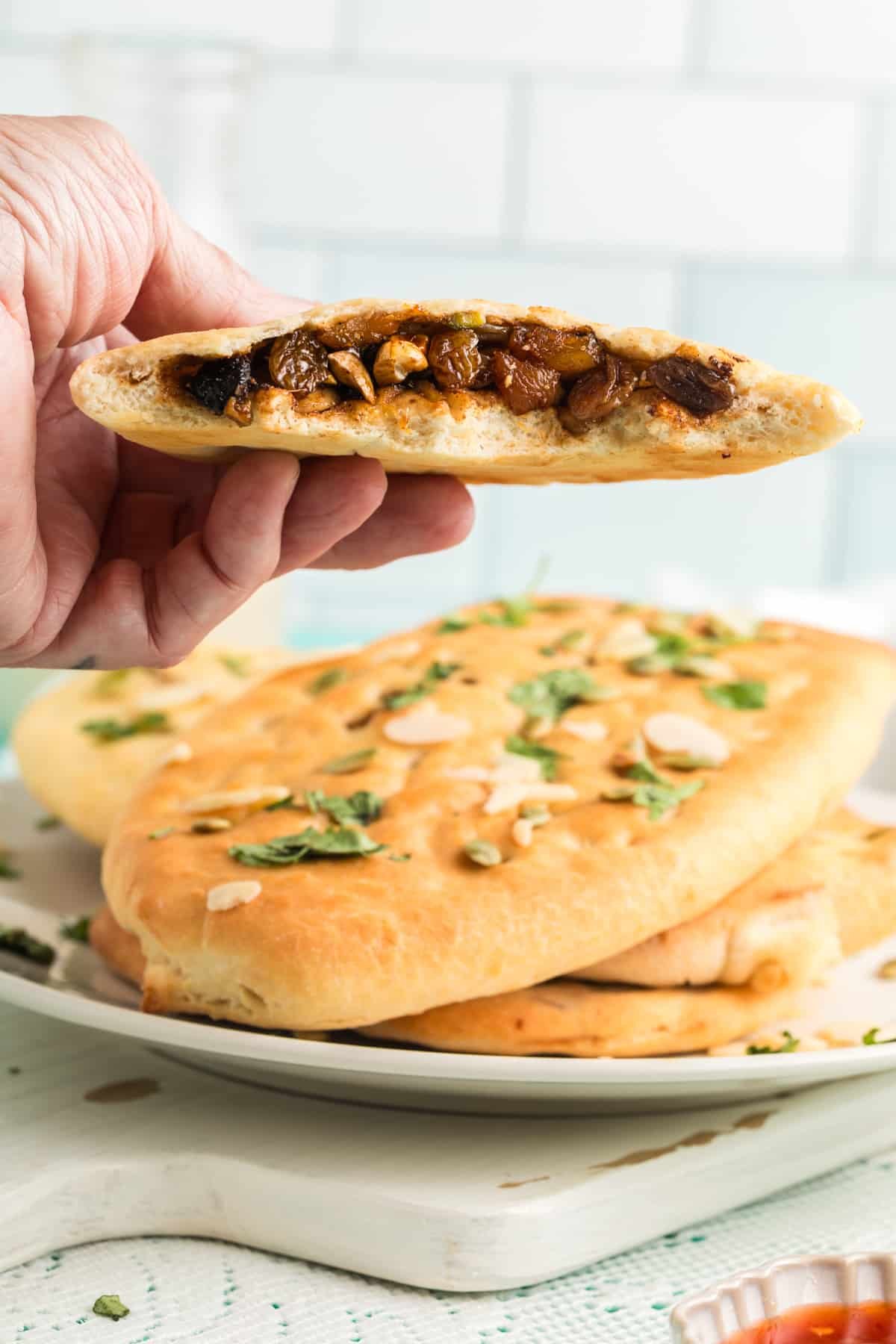 hand holding up a slices of Kashmiri Naan torn in half revealing the luscious filling