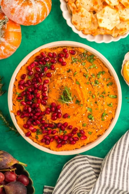 PUMPKIN HUMMUS RECIPE IN A WHITE BOWL ON A GREEN BACKGROUND