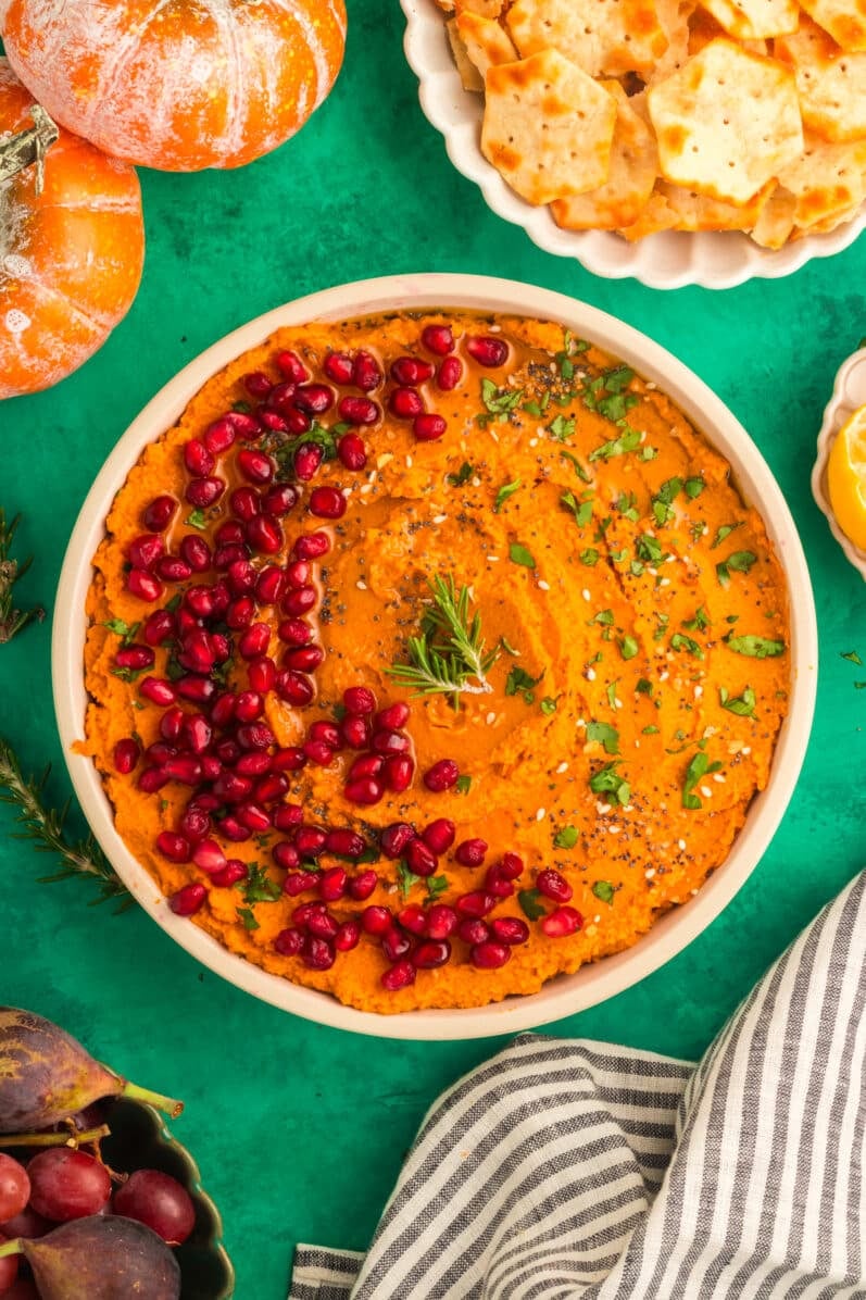 PUMPKIN HUMMUS RECIPE IN A WHITE BOWL ON A GREEN BACKGROUND