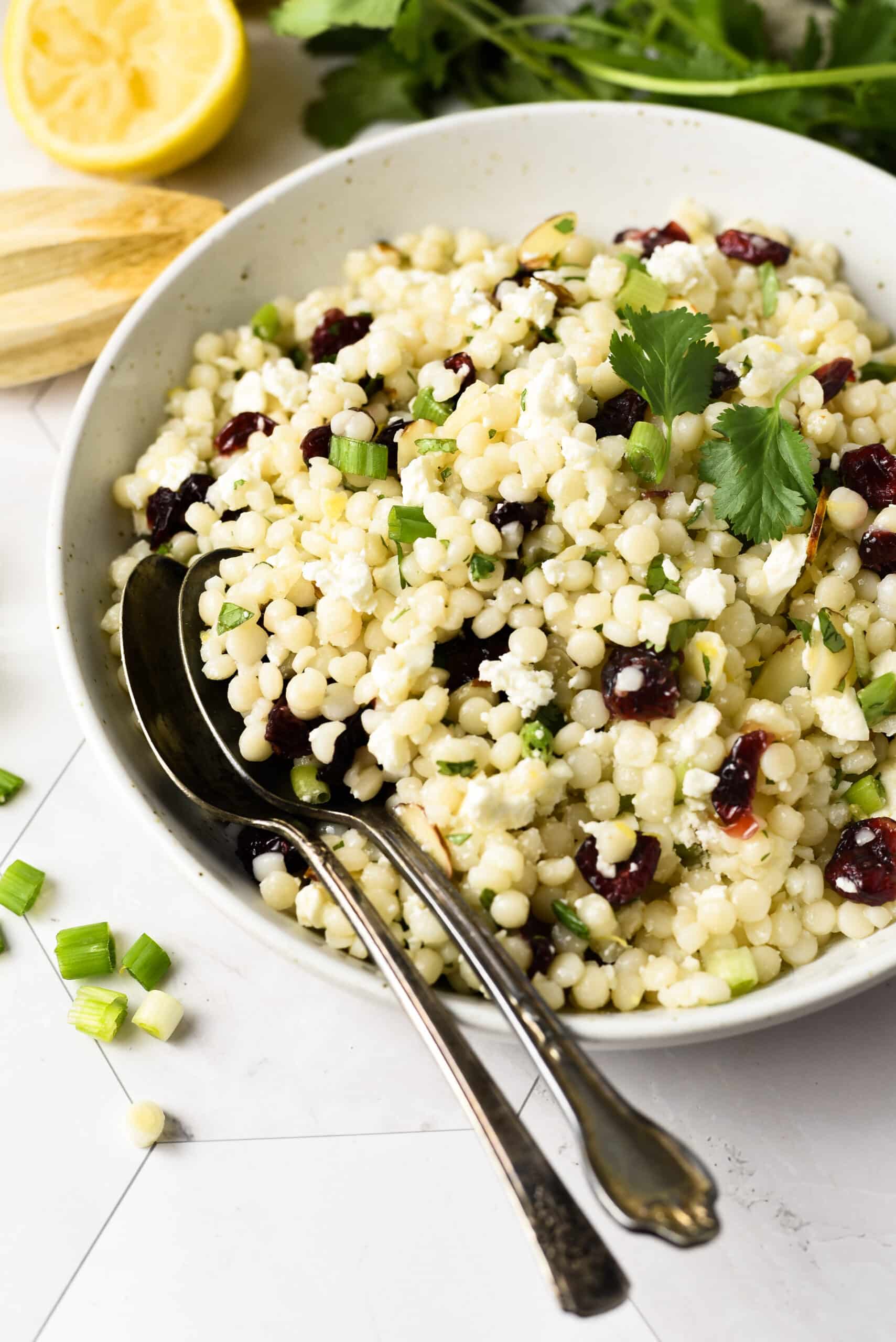 overhead side view of pearl couscous salad in a white plate with two forks