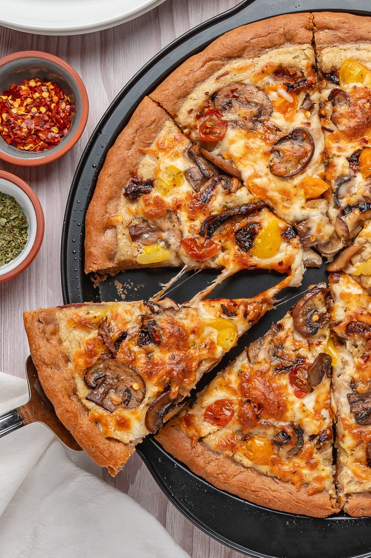 Slice of vegan pizza with cheese pull being removed from the pizza