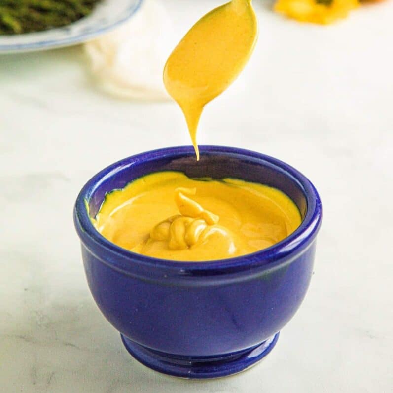 spoonful of yellow sauce dripping over a blue bowl